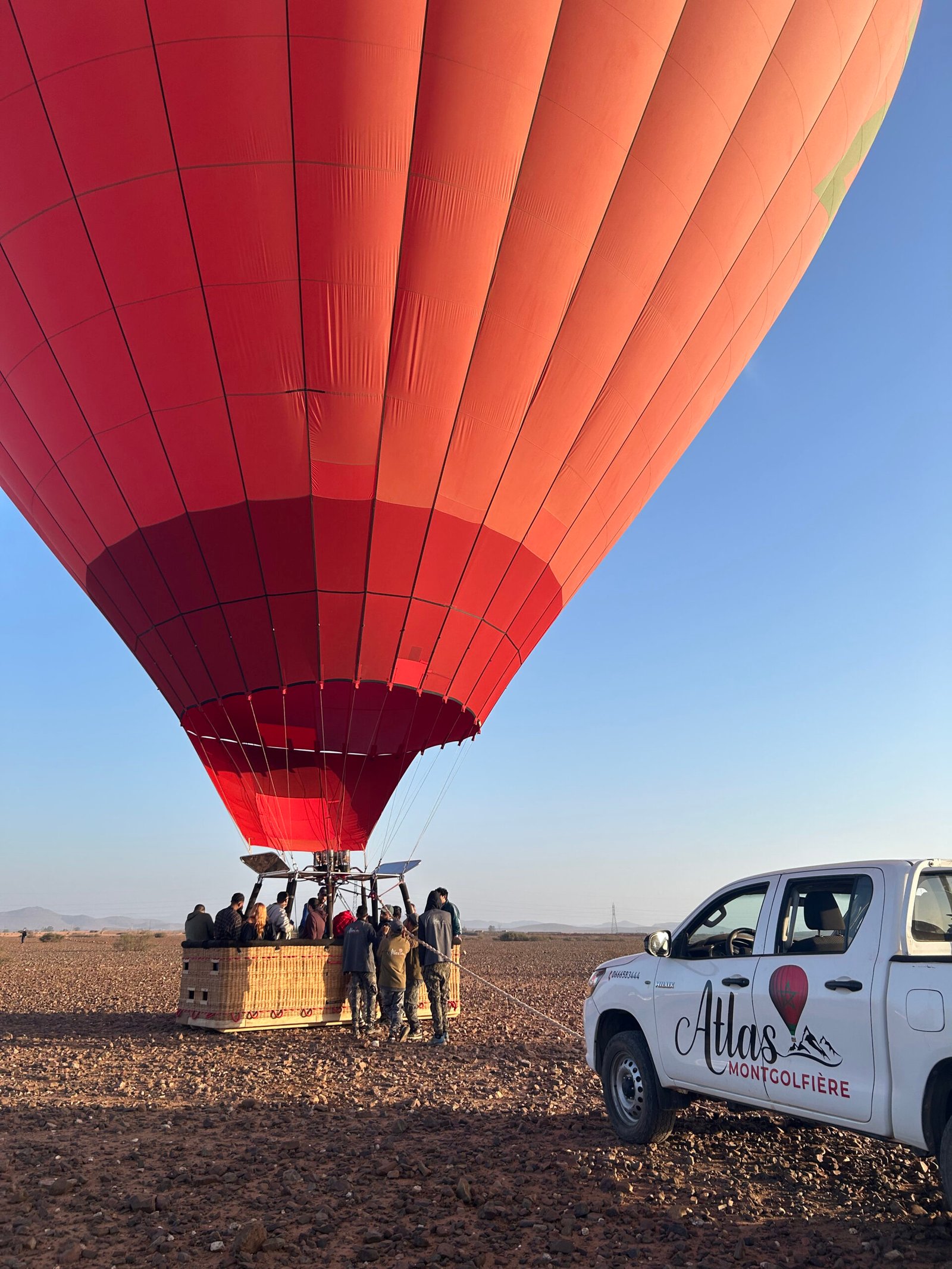 Une voiture à côté d’une montgolfière remplie de passagers prêts à embarquer.