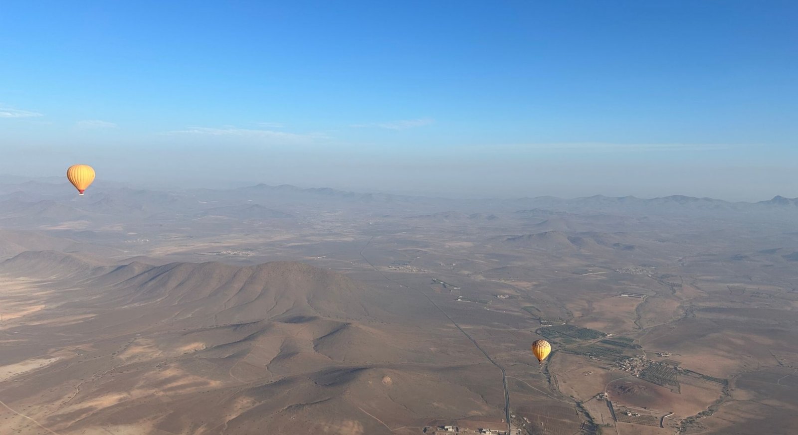 Montgolfière jaune dans le ciel au lever du soleil au-dessus du désert de Marrakech avec vue sur les montagnes de l’Atlas