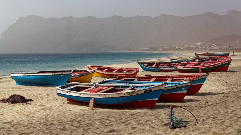 A scenic view of colorful fishing boats resting on a sandy beach next to a calm ocean.